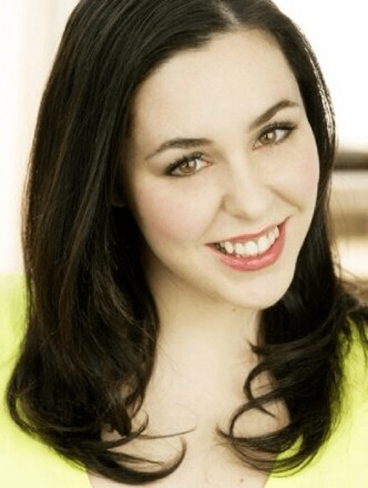 Bella Poynton, Smiling young woman with fair skin, long dark brown hair parted to the side, hazel eyes, subtle makeup, and soft red lipstick, wearing a bright yellow top against a light blurred background.